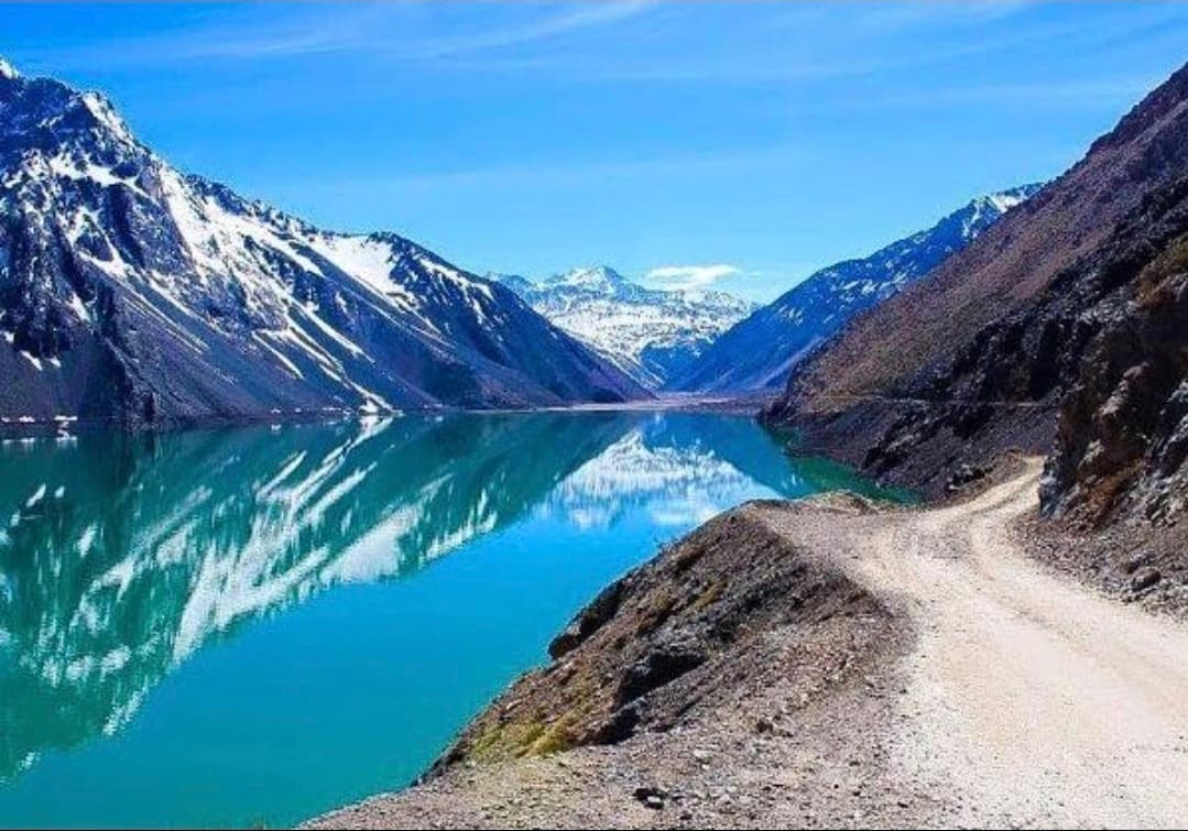 Embalse El Yeso de aguas turquesas entre cumbres nevadas y camino de ripio